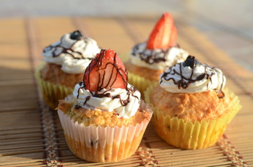 Four awesome cupcakes decorated with cream, berries and chocolate sauce