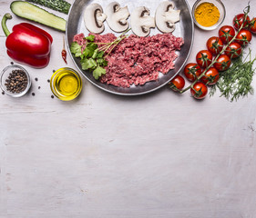 raw minced meat with mushrooms in a pan, pepper, tomatoes on a branch, spices, cucumbers  border ,with text area, on wooden rustic background top view