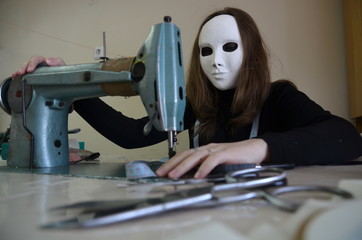 woman in a theatrical mask works on the sewing machine