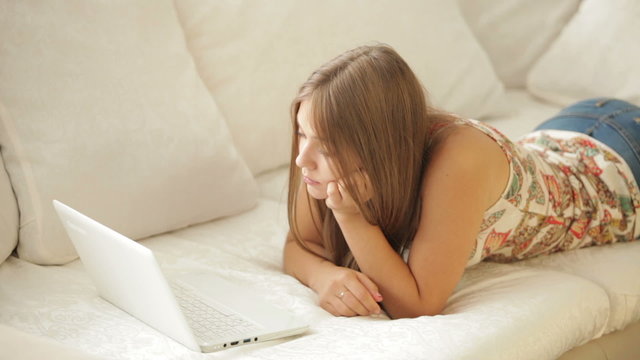 Young woman lying on sofa and using laptop