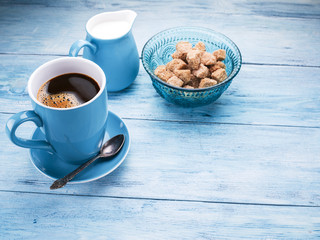Cup of coffee, milk jug and cane sugar cubes.