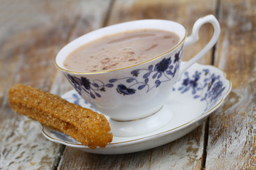 Spanish churro with cup of hot chocolate on rustic wooden surface
