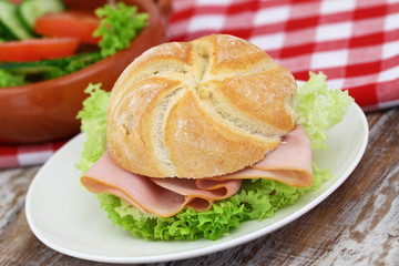 Bread roll with ham and lettuce on white plate, closeup
