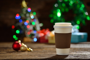Paper cup of coffee with smoke surrounded by Christmas decorations on Christmas lights bokeh background