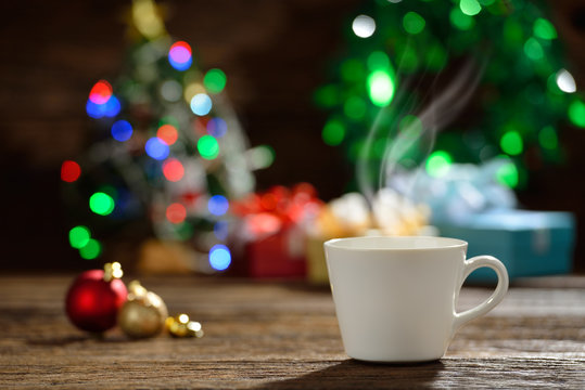 Cup of coffee with smoke surrounded by Christmas decorations on Christmas lights bokeh background