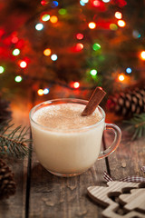 Homemade eggnog, egg milk vanilla rum, alcohol liqueur in glass with cinnamon stick on vintage wooden table. Colorful bokeh background, shallow depth of field