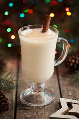 Eggnog christmass holiday traditional celebration milk cream drink in glass cup on vintage wooden table. Colorful bokeh and shallow depth of field