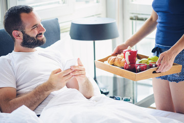 Woman is bringing man a breakfast in bed