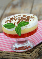 Strawberry trifle in dessert glass on checkered cloth on rustic wooden surface
