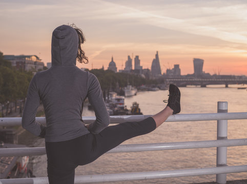 Fitness woman stretching leg on bridge at sunrise