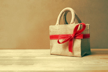 Beautiful gift bag with red bow on wood background and color filters