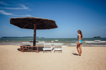 Woman on a tropical beach on deck chair under sun umbrella.woman resting under umbrella facing the seaside in a deserted beach with deep blue sky