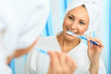 Young girl in a bathrobe holding a tooth brush and thinking in the bathroom