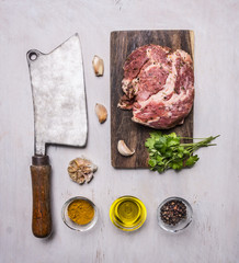 raw pork steak on a cutting board and vintage meat cleaver with spices, garlic and herbs on wooden rustic background top view close up