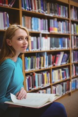 Pretty student sitting on chair holding book in library