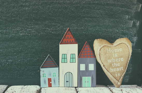 image of vintage wooden colorful house and fabric heart on wooden table in front of  blackboard. faded retro filtered image