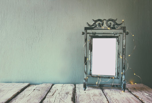low key image of old victorian steel blue blank frame with fairy garland lights. faded retro filtered image
