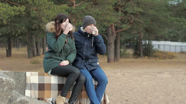 Healthy young couple taking time alone together wearing warm clothing sitting beach drinking coffee