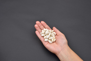 Hand of a woman holding a pile of dry white beans isolated on bl