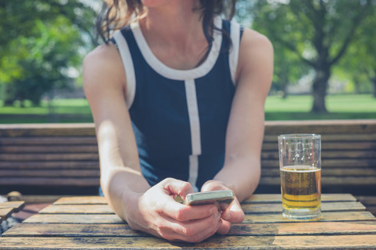 Young woman using smart phone and drinking beer
