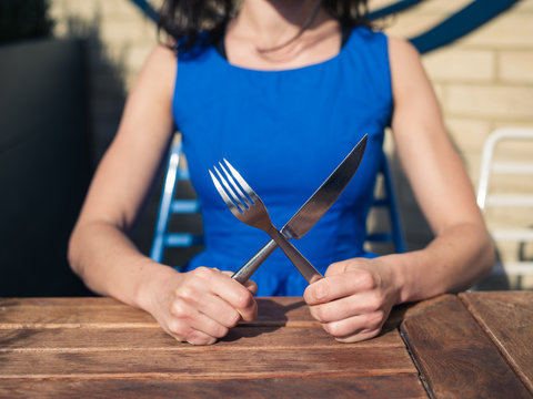 Young woman sitting at table with fork and knife