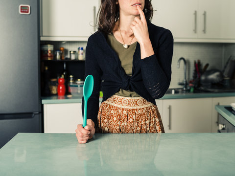 Confused woman with spoon in kitchen