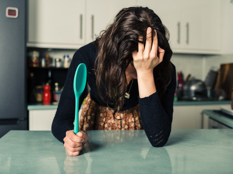 Sad woman with spoon in kitchen