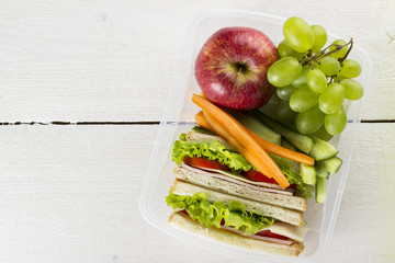 Lunchbox with sandwich, vegetables, fruit on white background.