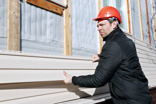 A worker installs panels beige siding on the facade of the house