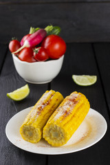 Corn with various vegetables and lime on a wooden background