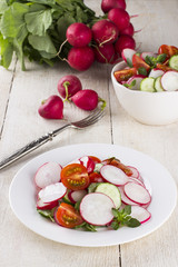 Salad with radish, cherry tomatoes and cucumber on white wooden