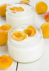 Yogurt in two glass jars with apricots on white background