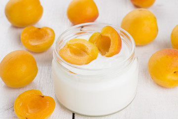 Yogurt in glass jar with apricots on white wooden background