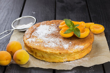 Cottage cheese pie, apricots and icing sugar on a brown wooden b