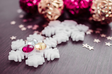 White snowflakes on background of magenta and gold xmas baubles with space for text. Merry christmas. Winter holidays. Xmas theme. Happy New Year. Blurred background.
