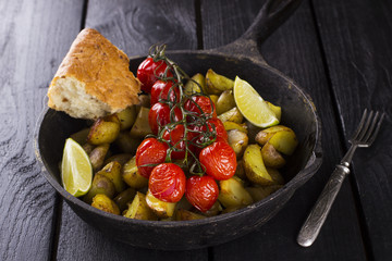 Frying pan with fried potato and the baked cherry tomatoes on br