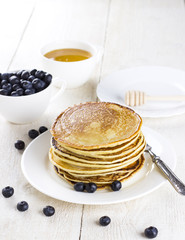heap of pancakes on a white plate with blueberry on a white wood