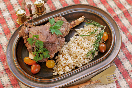 Baked lamb leg on plate with  brown organic rice tomatoes, ,parsley