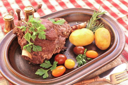 Baked lamb leg on plate with tomatoes,  potato ,parsley