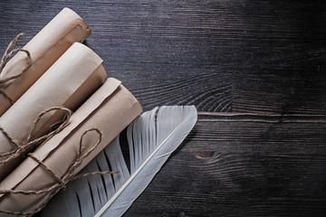 Rolled up vintage papers with feather on wooden board