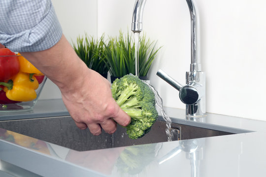 man  washing broccoli   with water in kitchen