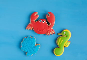 Homemade homemade gingerbread cookie in the shape of grteen sea Horse, crab and shell on a blue wooden background. Space for text and selective focus.