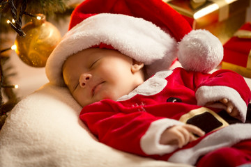 Fototapeta na wymiar baby boy in Santa costume lying under Christmas tree. Christmas