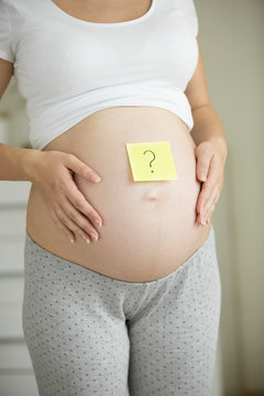 Closeup of pregnant with question mark drawn on post-it sticker