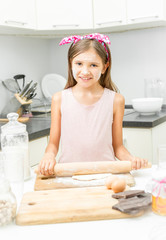 smiling girl rolling dough on messy kitchen