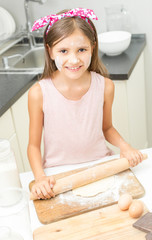 smiling cute girl rolling dough with wooden pin on kitchen