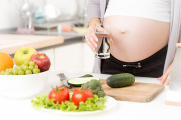 Obraz na płótnie Canvas Closeup of pregnant woman holding glass of water on kitchen