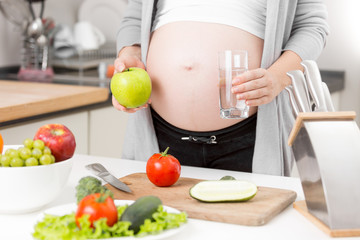 Closeup of pregnant woman having apple and water for breakfast