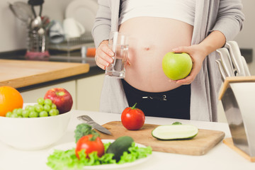 Obraz na płótnie Canvas Closeup of pregnant woman posing on kitchen with apple and glass