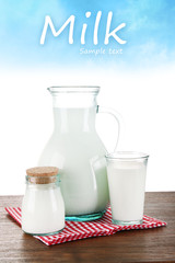Pitcher, jar and glass of milk on light blue background